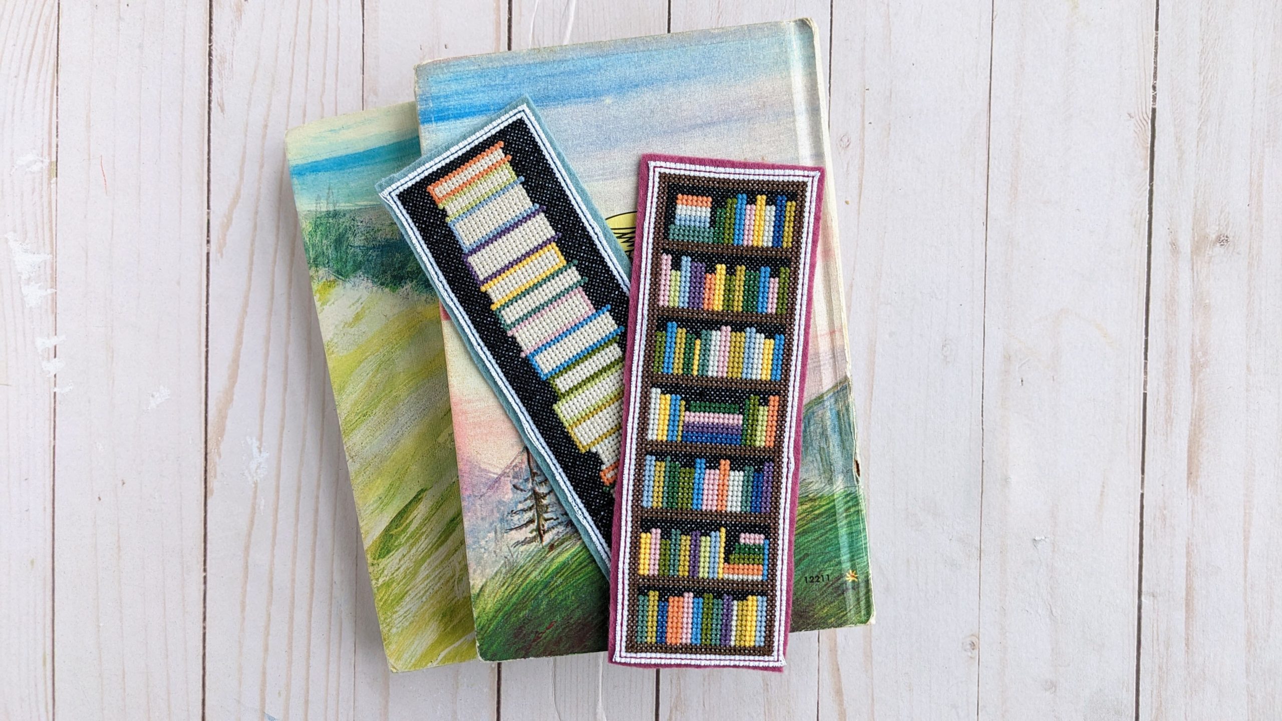 two cross stitched bookmarks on top of vintage books